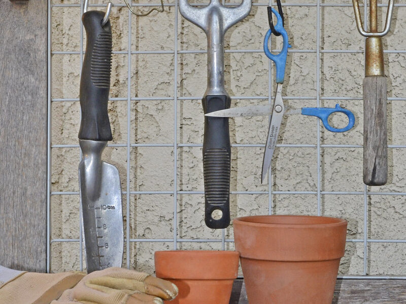 Well-used hand gardening tools, gloves and terracotta pots on a potting bench — garden maintenance gear